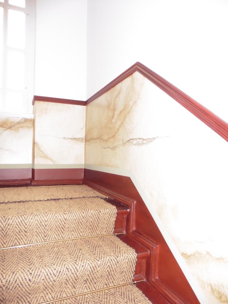 Restaurator Schimpf hat im Denkmal Treppenhaus Charlottenburg im Paneelbereich eine Marmorimitation mittels einen Kalkspachtel und Lasuren in verschiedenen Schichten angebracht. Dabei hat er sich an historische Vorgaben gehalten. In diesem Treppenhaus aus Berlin der Gründerzeit wurde neben der Marmormalerei auch Lasurarbeiten bzw. Lasurtechniken an den Türen aufgearbeitet. Hier wurde eine Patina imitiert. Ebenso wurden alle Traljen durch eine Lasur in ihren alten Glanz abgearbeitet.  Der Restaurator und Malermeister Schimpf hat viele Treppenhäuser in Berlin Kreuzberg, Prenzlauer Berg, Charlottenburg überarbeitet. Meist werden im historischen Treppenhaus aus dem Jugendstil und der Gründerzeit Deckenmalerei, Kalkspachtel, Spachteltechnik, Schablonentechnik historische Maltechniken Marmormalerei, Holzimitation oder Holzmalerei und Wandmalerei angebracht. Restaurator Schimpf nimmt am Denkmal die historischen Farben – Farbmaterialien wie Ölfarben und Temperamischung oder Knochenleim wieder auf.